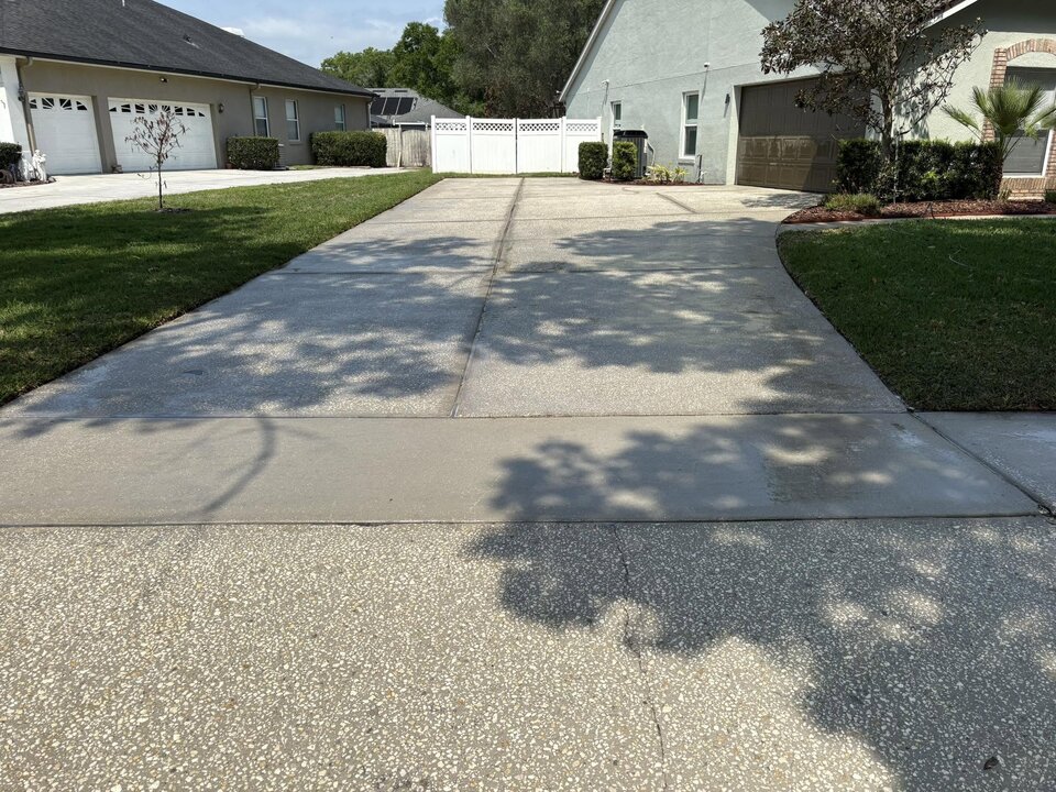 Long concrete driveway in Oviedo FL gleaming in the sun after professional pressure washing, leading to a white vinyl gate
