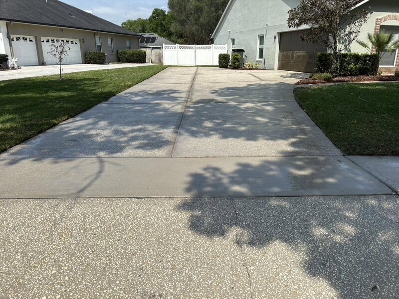 Bright, uniformly clean long driveway leading to a white vinyl gate after pressure washing