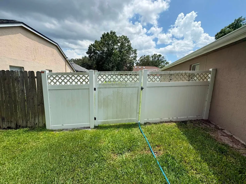 White vinyl lattice-top fence and gate stained with green algae before cleaning