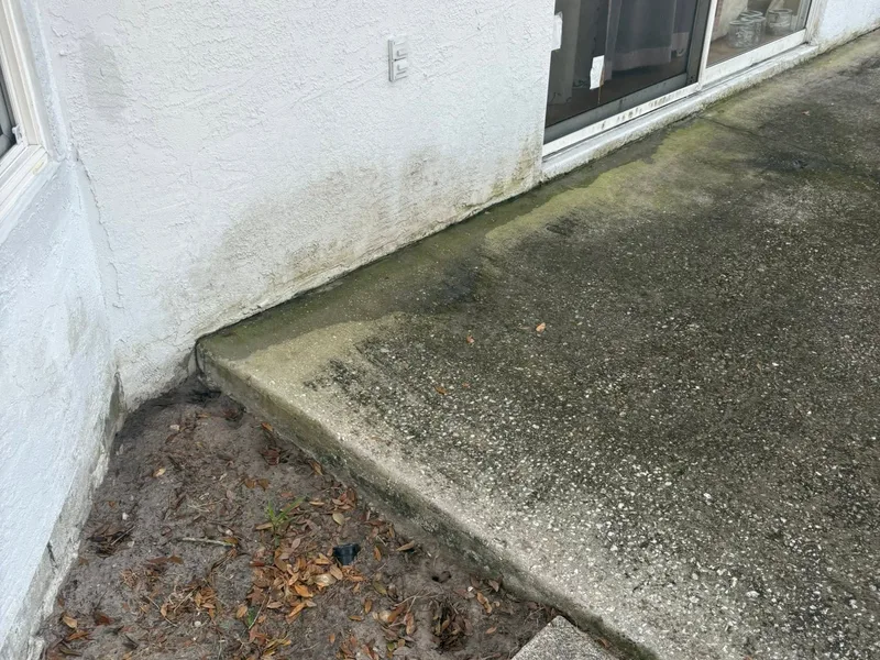 Green-stained grimy patio corner at a sliding glass door before washing