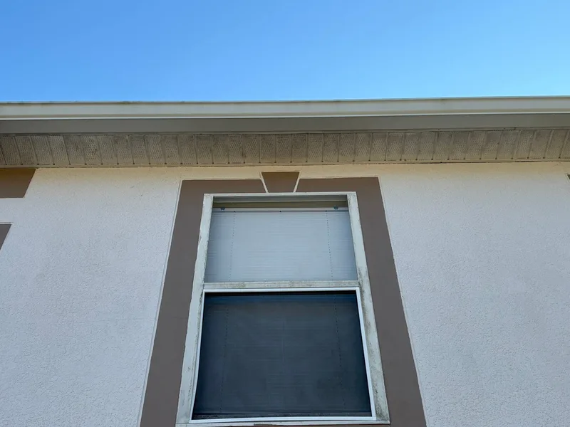 Second-story window with grimy frame and dirty soffit before soft washing