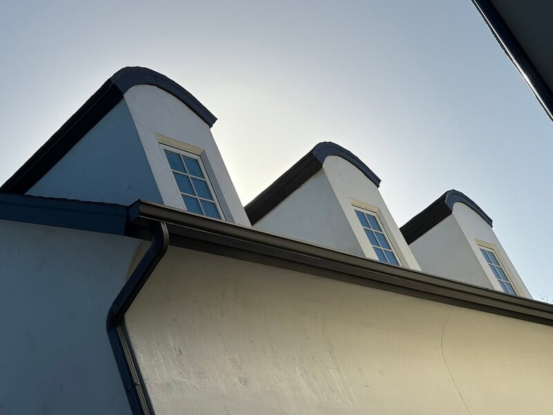 Three clean white stucco dormers against a clear sky after soft washing