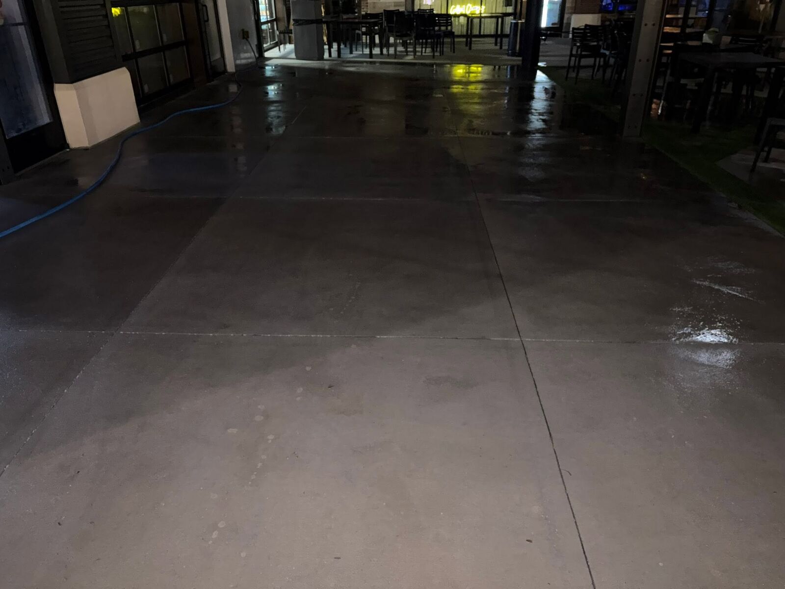 Freshly washed dining courtyard glistening under neon restaurant lights during an overnight pressure wash at the Food Factory